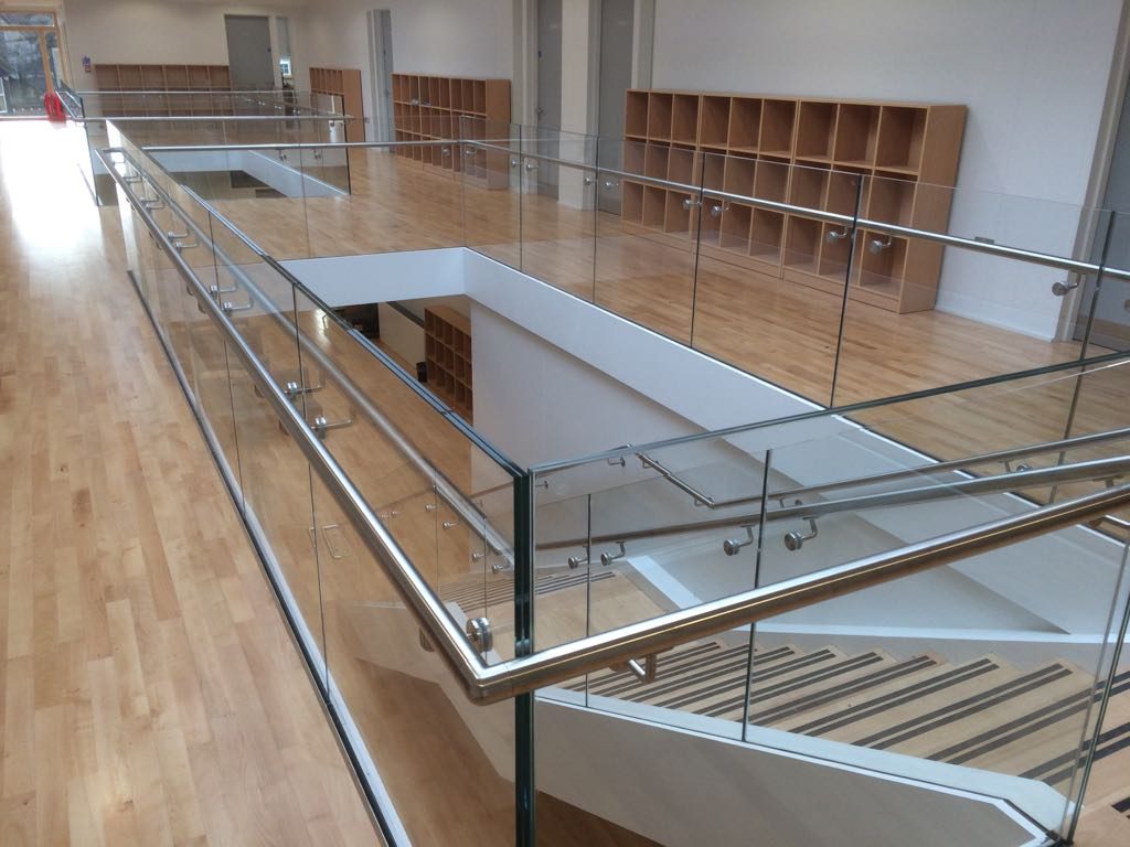 Glass balustrade with stainless steel handrail around a first-floor atrium landing above a staircase