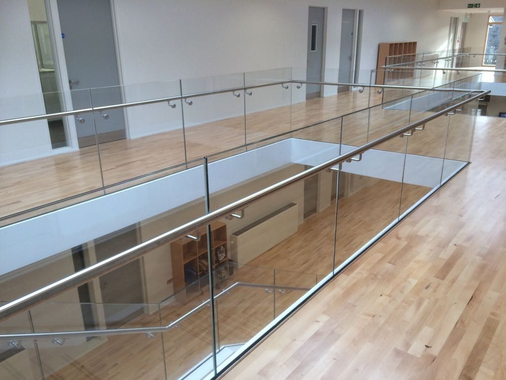 Glass balustrade and stainless steel handrail running along a first-floor landing with a maple floor