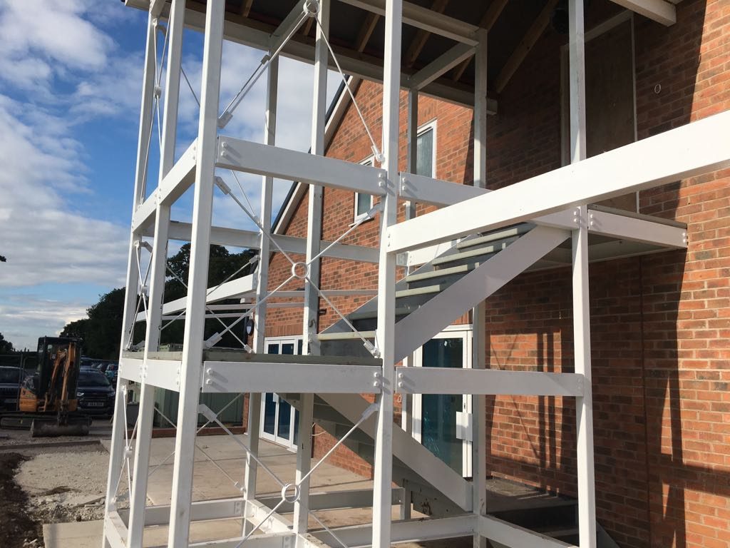 White-painted structural steel framework being erected against a brick building, with cross-bracing and tie rods in place